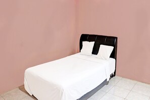 A single bed with a black headboard in a room with pink walls and tiled flooring.