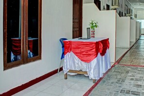 A hallway with a table covered in a red and white cloth, a vase with flowers, and a blue chair. - Oyo 91416 Puri 88 Homestay (Kupang)
