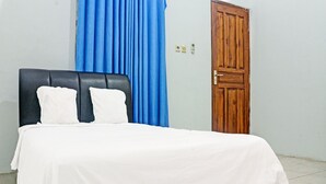 Un lit avec une tête de lit noire, du linge de lit blanc et un rideau bleu.