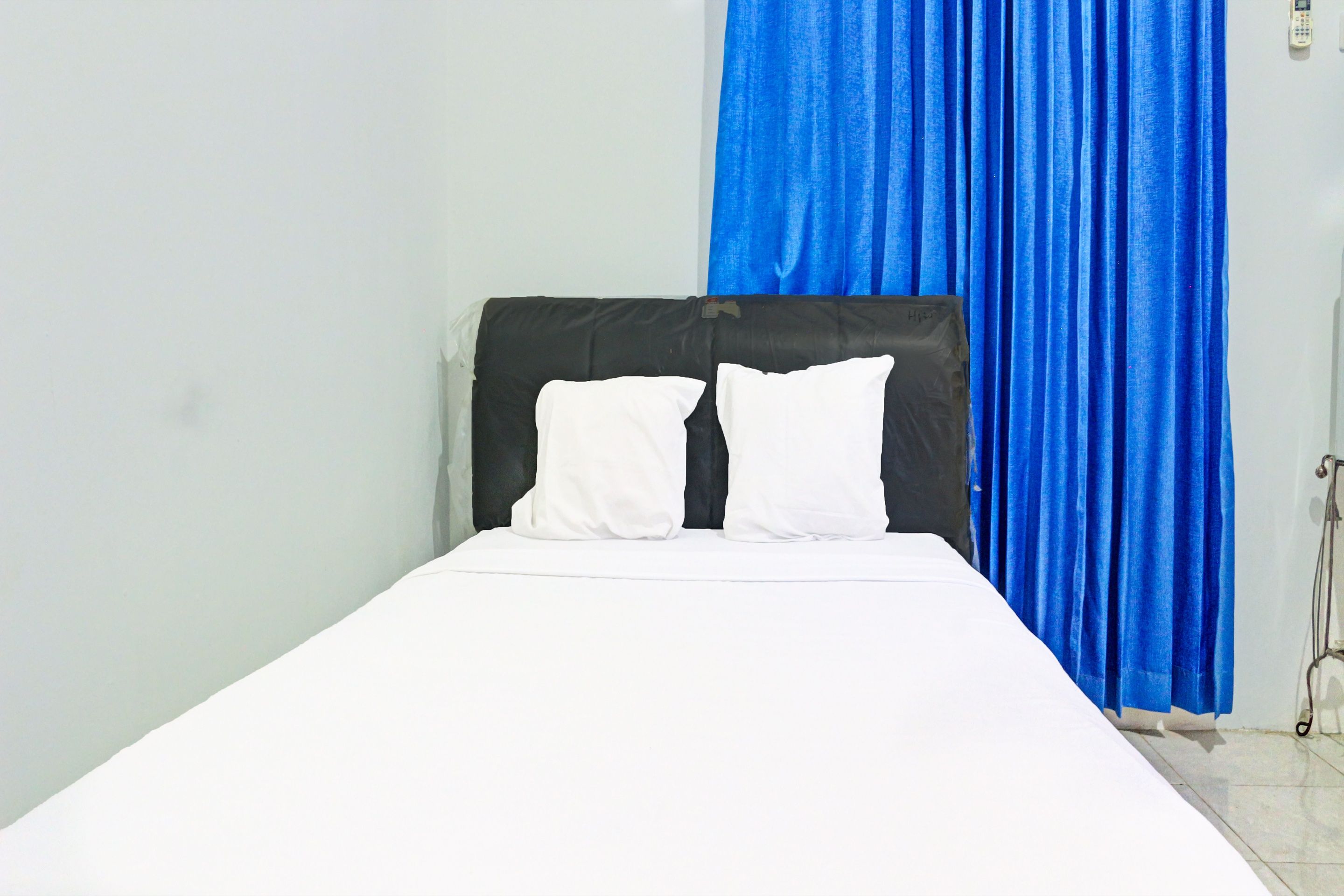 A single bed with white bedding, a black headboard, and a blue curtain.