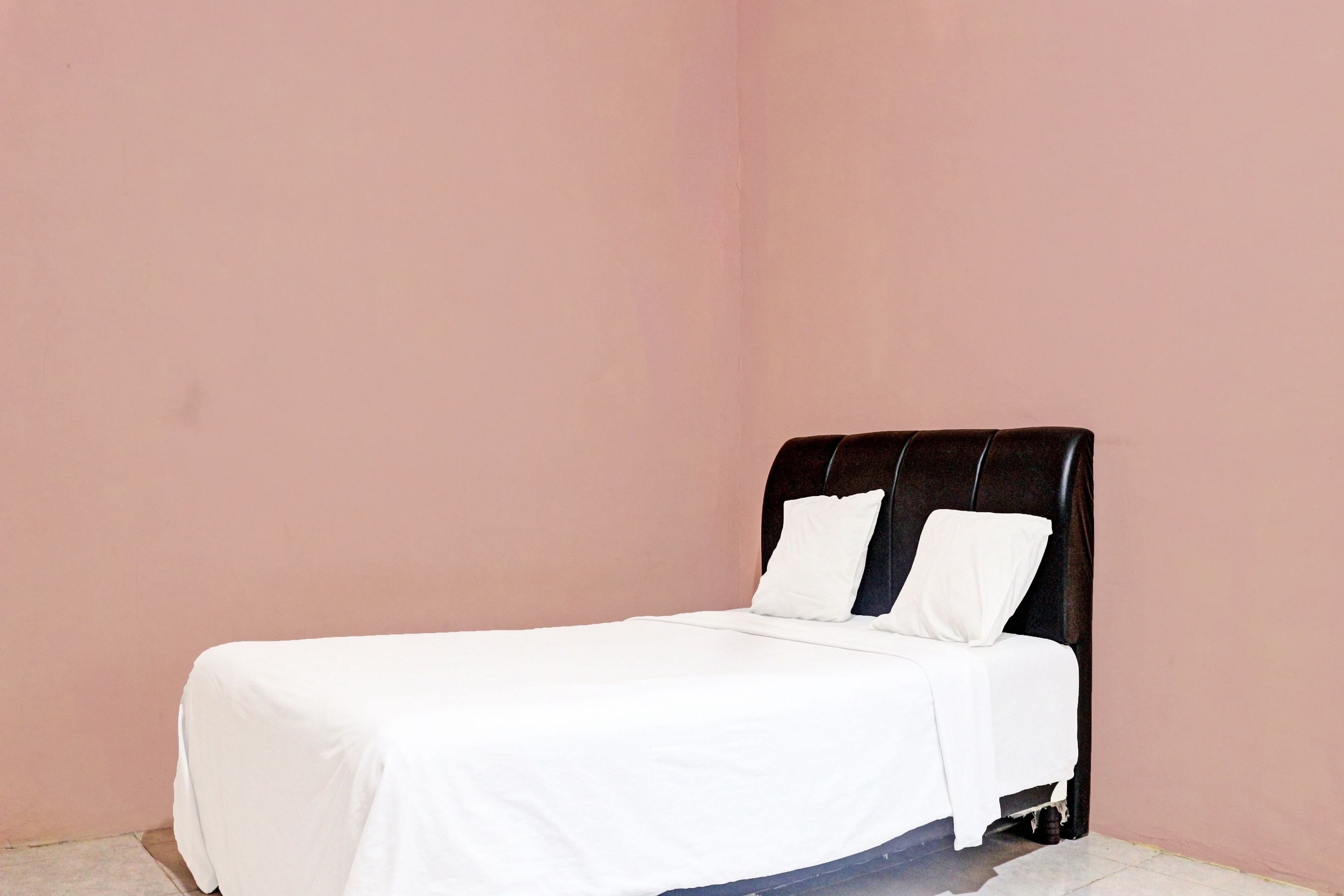 A single bed with a black headboard in a room with pink walls.