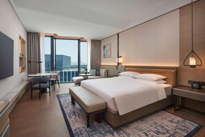 Habitación de hotel con una cama grande, un escritorio, una silla, una mesita, un sofá y vistas a la ciudad.