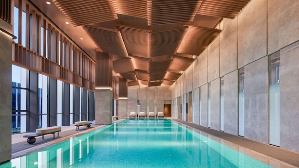 Una amplia piscina cubierta con diseño moderno, rodeada de grandes ventanales y un techo alto con listones de madera.