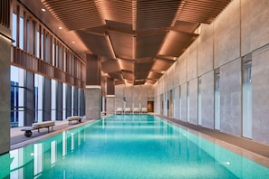 Una amplia piscina cubierta con diseño moderno, rodeada de grandes ventanales y un techo alto con listones de madera.