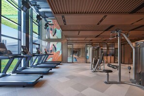 Un gimnasio con cintas de correr, máquinas de pesas y un ventanal con vista a zonas verdes.