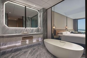 A modern hotel room with a large oval bathtub, a marble vanity, a large mirror, and a bed with a view of the city. - Hyatt Regency Hangzhou Intl Airport (Hangzhou)