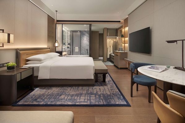 Una habitación de hotel moderna con una cama grande, mesita de noche, lámpara y televisor.