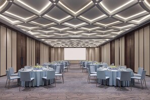 Un salón de conferencias con mesas redondas, sillas y una pantalla grande al frente.