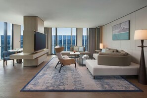 Una habitación de hotel moderna con un televisor grande, asientos cómodos, una mesa de centro y vistas a la ciudad.