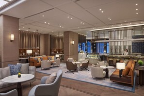 Eine moderne Hotelhalle mit Sitzbereichen, einem Empfangsbereich und einer Küche im Hintergrund.