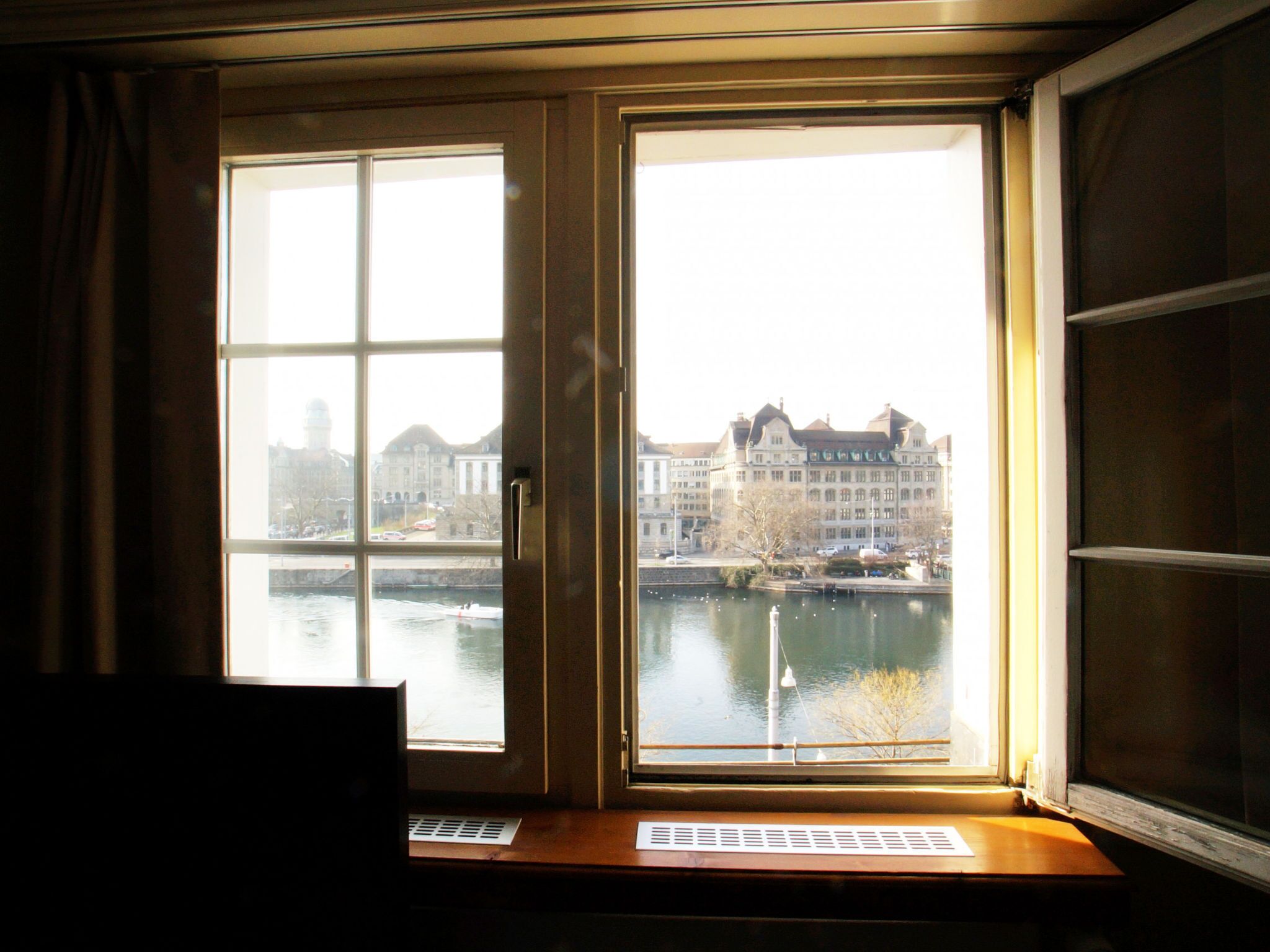 Ein Zimmer mit großem Fenster und Blick auf einen Fluss und Gebäude.