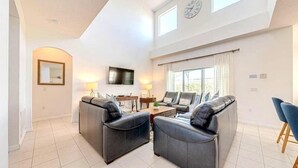 A spacious living room with a sofa set, a flat-screen TV, and a large window with curtains. - Legacy Park Executive Gamesroom (Davenport)