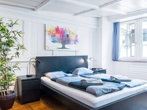 Un dormitorio moderno con una cama, mesitas de noche, una planta en maceta y un cuadro abstracto colorido en la pared.