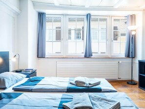 Ein Hotelzimmer mit Bett, Nachttisch, Lampe und Blick ins Freie durch ein Fenster.