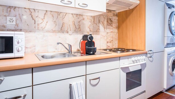 Ett modernt kök med mikrovågsugn, vattenkokare, diskho, spis, ugn och tvättmaskin.