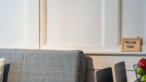 Ett rum med en grå soffa, ett litet bord med en skål med frukt och en skylt på väggen med texten ”Välkommen hem”.