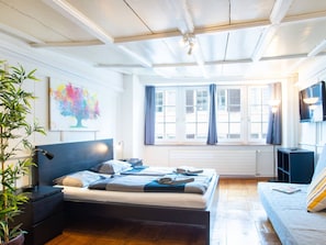 A modern bedroom with a bed, bedside tables, a TV, and a window with curtains. - Apartment  by Interhome (Zurich)