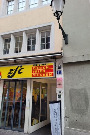 Un edificio con un cartel que dice 'Original Zurich Fried Chicken' y un letrero de 'Hair Lounge'.