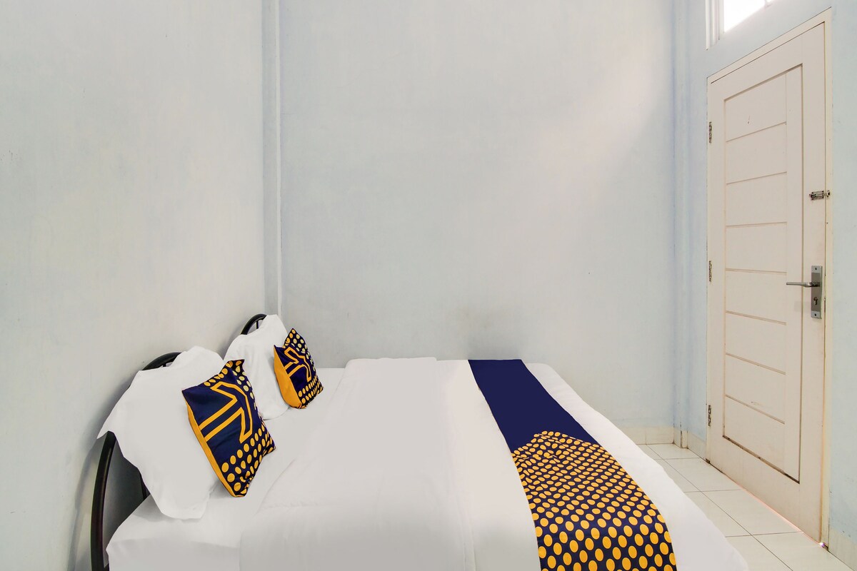 Una cama con ropa blanca, dos almohadas con diseños amarillos y azules, y una manta a rayas azul y amarilla.