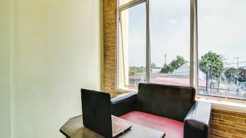 A room with a laptop on a table, a red chair, and a large window offering a view of the street and buildings outside.