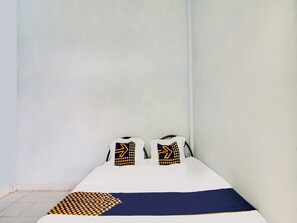 Um quarto pequeno e simples com uma cama, duas almofadas e um cobertor.