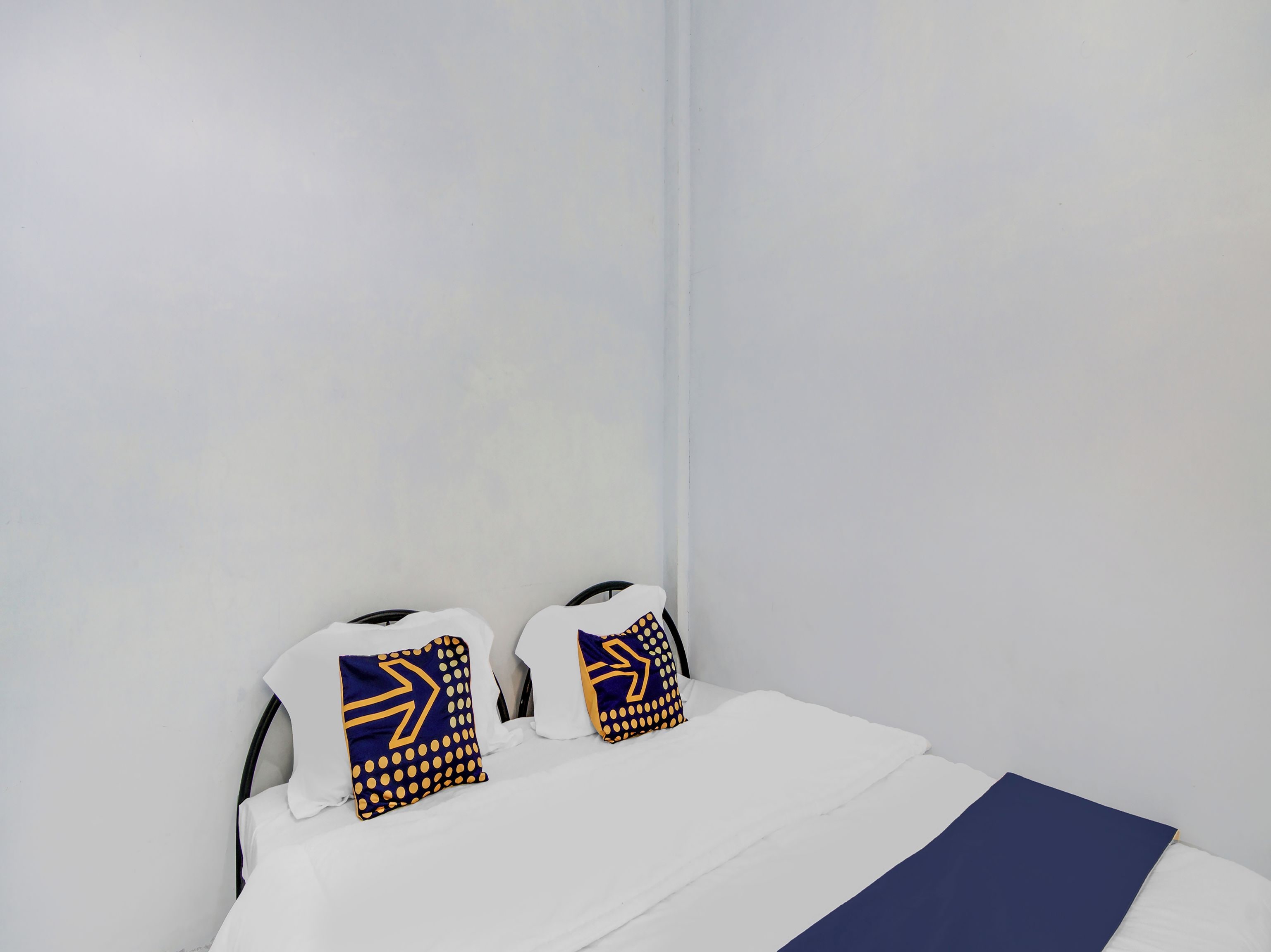 A bed with white bedding and two pillows with blue and yellow patterns.