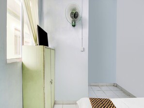 Una habitación con un armario verde, una cama con una colcha de lunares, un ventilador de pared y una ventana con cortinas.