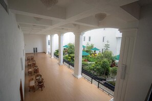A spacious indoor area with a balcony overlooking a garden, featuring columns and a wooden floor. - Araliya Red (Nuwara Eliya)