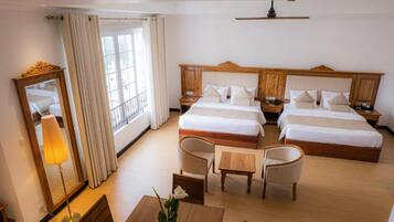 A hotel room with two beds, a sitting area with a table and chairs, a mirror, and a window with curtains.