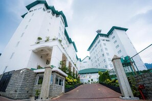 A white building with a green roof and multiple windows, featuring a stone entrance and a paved pathway leading to the entrance. - Araliya Red (Nuwara Eliya)