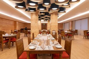 A restaurant with wooden walls and ceiling, multiple dining tables, and red cushioned chairs. - Araliya Red (Nuwara Eliya)