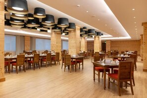 A spacious dining area with multiple tables and chairs, wooden pillars, and modern pendant lighting. - Araliya Red (Nuwara Eliya)