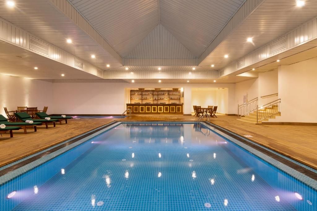 An indoor swimming pool with a tiled floor, lounge chairs, and a reception area with a counter.