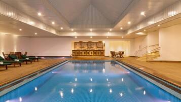 An indoor swimming pool with a tiled floor, lounge chairs, and a reception area with a counter.