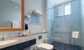 A bathroom with a granite countertop sink, a white toilet, a glass-enclosed shower, and a mirror with a wooden frame. - Araliya Red (Nuwara Eliya)