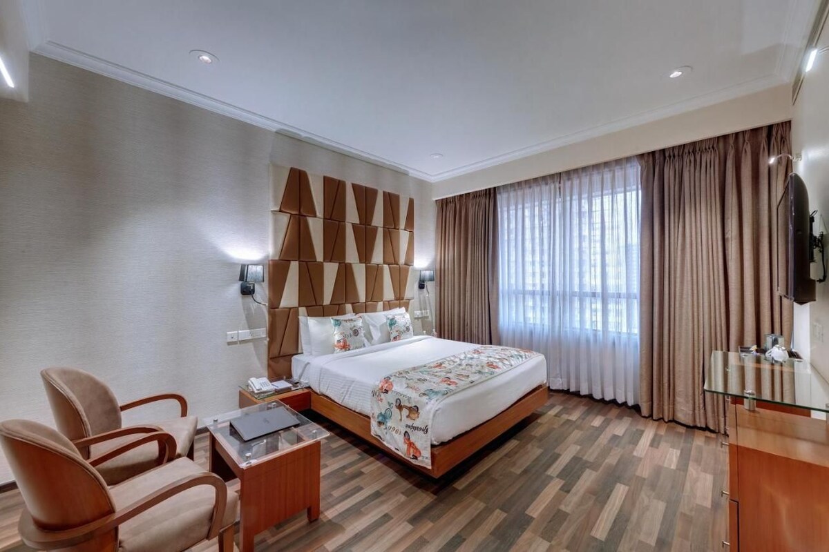 A hotel room with a bed, a desk, a chair, a TV, and a large window with curtains.