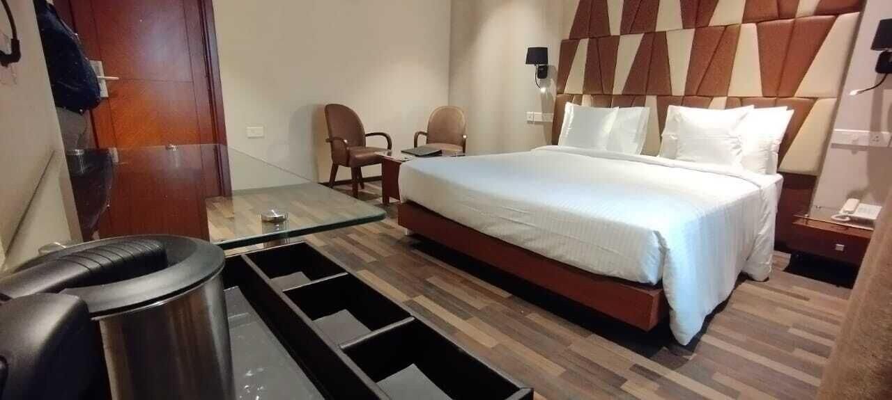 A hotel room with a bed, two chairs, a small table, a trash bin, and a nightstand with a phone.