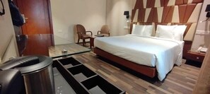 A hotel room with a bed, two chairs, a small table, a trash bin, and a nightstand with a phone. - Adiva Residency Beacon,mumbai (Mumbai)