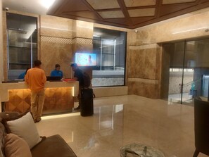 A reception area with a marble wall, a digital screen, and a glass door leading outside. - Adiva Residency Beacon,mumbai (Mumbai)