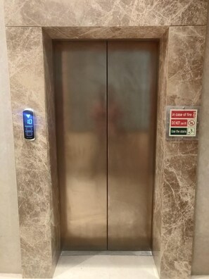 An elevator with a digital display, marble walls, and a fire safety sign. - Adiva Residency Beacon,mumbai (Mumbai)
