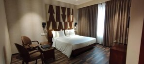 A hotel room with a bed, a desk, a chair, and a large window with curtains. - Adiva Residency Beacon,mumbai (Mumbai)