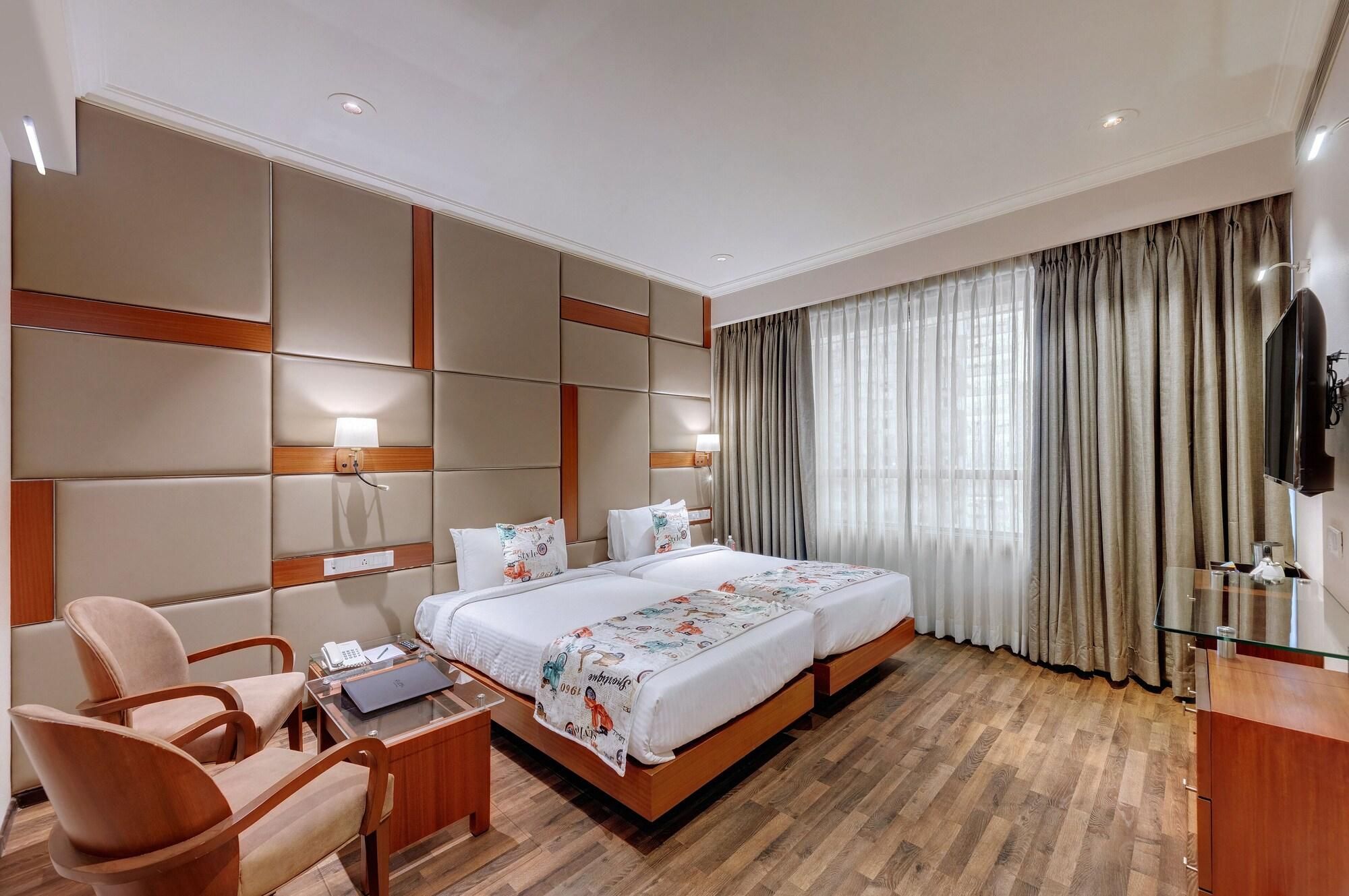 A hotel room with a large bed, a desk with a laptop, a chair, and a TV.