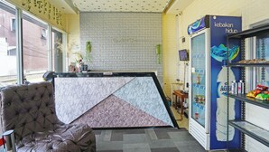 A hotel reception area with a marble counter, a plush seating area, a wall-mounted TV, and a vending machine.