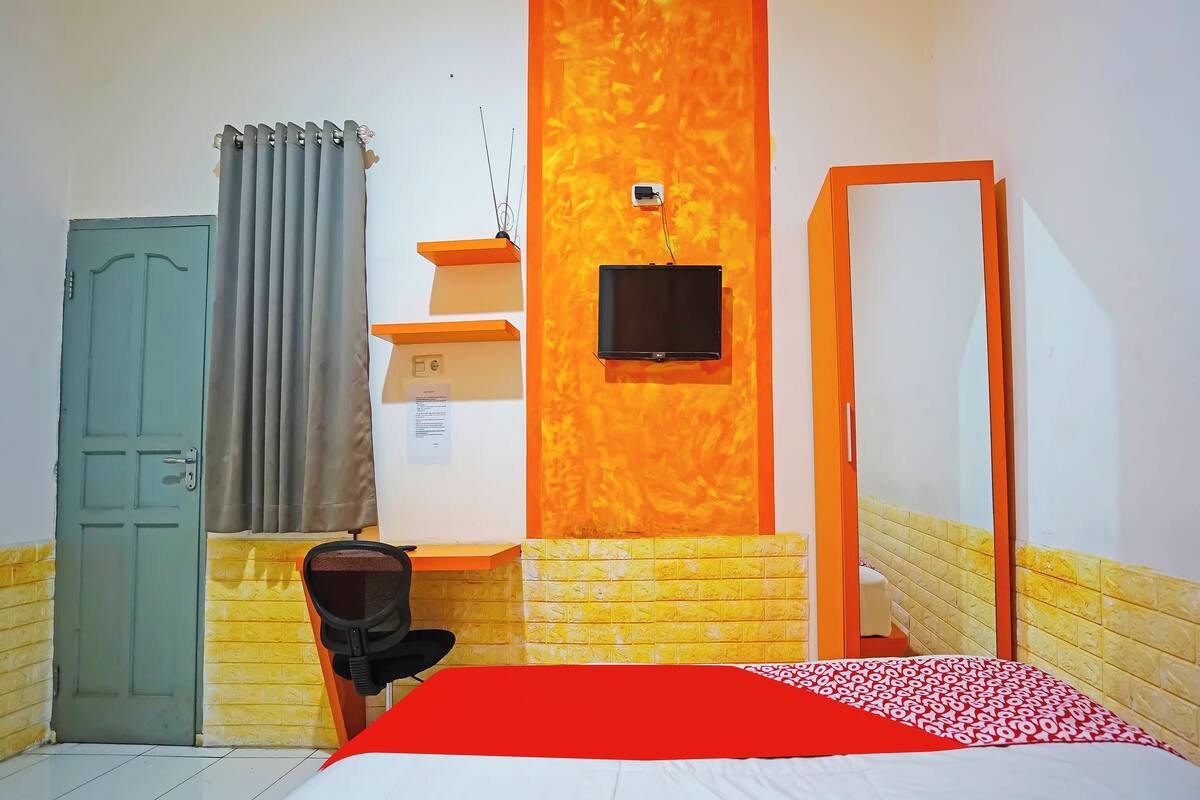 Een kamer met een bed, een bureau, een stoel, een televisie en een deur.