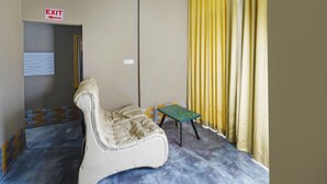 A room with a plush chair, a small table, a yellow curtain, and an exit sign.