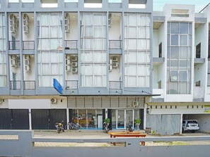 Um edifício de vários andares com aparelhos de ar condicionado, uma placa azul e uma moto estacionada na frente.