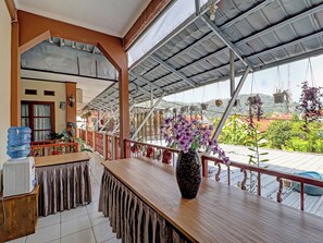 A covered outdoor seating area with a wooden table, a vase with flowers, and a view of greenery and buildings. - Oyo 91480 Putridapisa Syariah (Bangil)