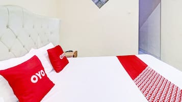 A hotel room with a white bed, red pillows, and a patterned bedspread.