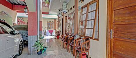A corridor with a car parked on the left, wooden chairs and tables along the right, and a wooden door with the number 11.