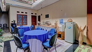 A dining area with round tables covered in blue tablecloths, chairs, a water dispenser, a refrigerator, and a decorative vase. - Oyo 91480 Putridapisa Syariah (Bangil)